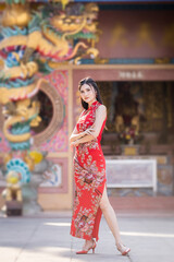 Portrait beautiful smiles Asian young woman wearing red traditional Chinese cheongsam decoration for Chinese New Year Festival at Chinese shrine in Thailand