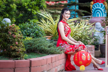 Asian woman wearing red traditional Chinese cheongsam decoration hold paper lanterns with the...
