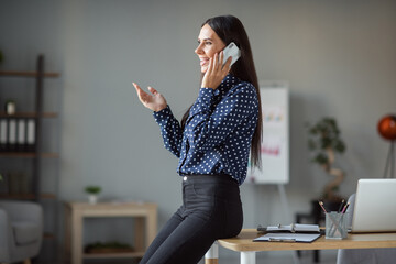 Profile side photo of attractive young woman sit on table talk smartphone client indoors workplace...