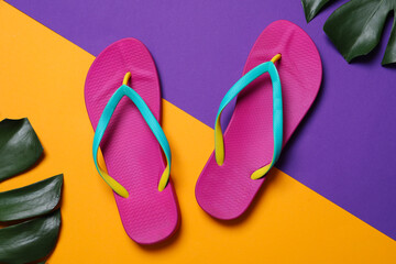 Bright flip flops and green leaves on color background, flat lay