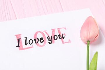 Card with text I Love You and tulip on pink wooden background, closeup