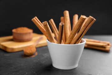 Aromatic cinnamon sticks in bowl on black table