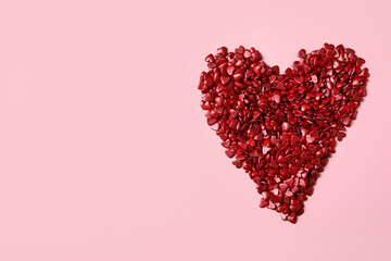 Heart made with red sprinkles on pink background, top view. Space for text