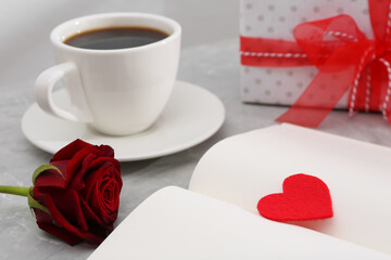 Open notebook with red heart, coffee and rose flower on light grey table. Valentine's day celebration