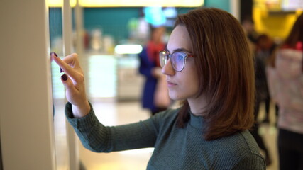 A young woman orders food at the touch terminal in a shopping center. Modern technology. On the...