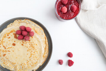 Pancakes in a plate and jam on a white wooden background with space for text. Pancake week.