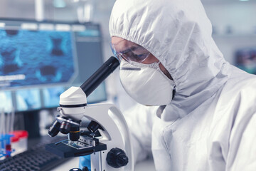 Doctor developing vaccine using microscope in modern laboraory. Virolog in coverall during...