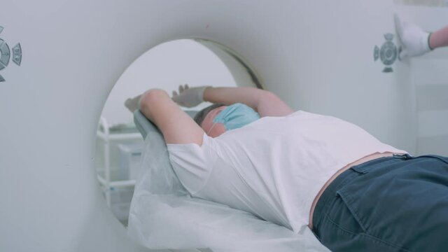 A patient in a protective medical mask lies in a modern computed tomography apparatus. The doctor analyzes the lungs on a CT scanner. The danger of covid or coronavirus. Human lung scans