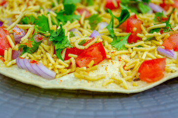 North Indian Snacks Masala Papad spread with sev, tomato, onions and Coriander leaves