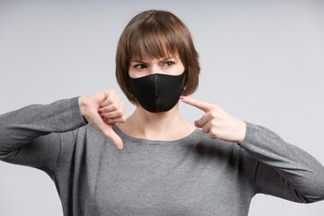 young woman points to her non medical face mask and shows thumbs down