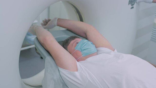 A patient in a medical mask is lying at a modern computer tomography machine. The doctor analyzes the lungs on a CT scanner. The danger of covid or coronavirus. Examining the organ of the lungs