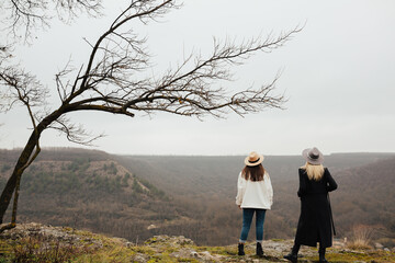 Full length back view of stylish girls standing on viewpoint and enjoying picturesque landscape.