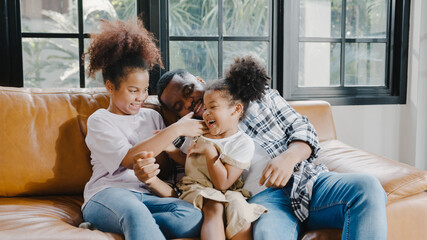 Happy cheerful African American family dad and daughter having fun cuddle play on sofa while...