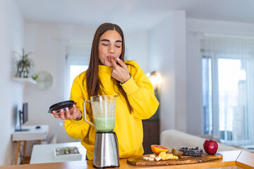 Healthy woman enjoy making green vegetables detox cleanse and green fruit smoothie with blender in kitchen at home. Healthy lifestyle. Beautiful girl tasting smoothie