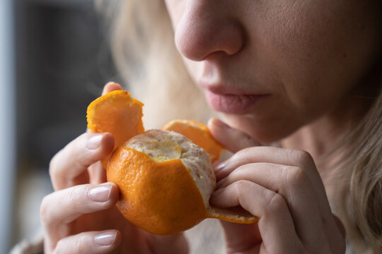 Sick woman trying to sense smell of fresh tangerine orange, has symptoms of Covid-19, corona virus infection - loss of smell and taste, standing at home. One of the main signs of the disease.