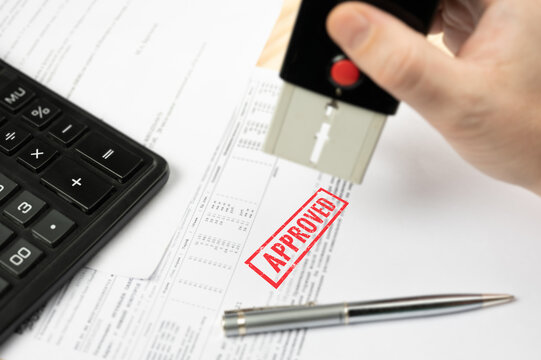 Approved Stamp. Close-up Of A Businessperson's Hand Stamping On Approved Contract Form. Tender Acceptance - Hand Put Approved Stamp On Financial Bill