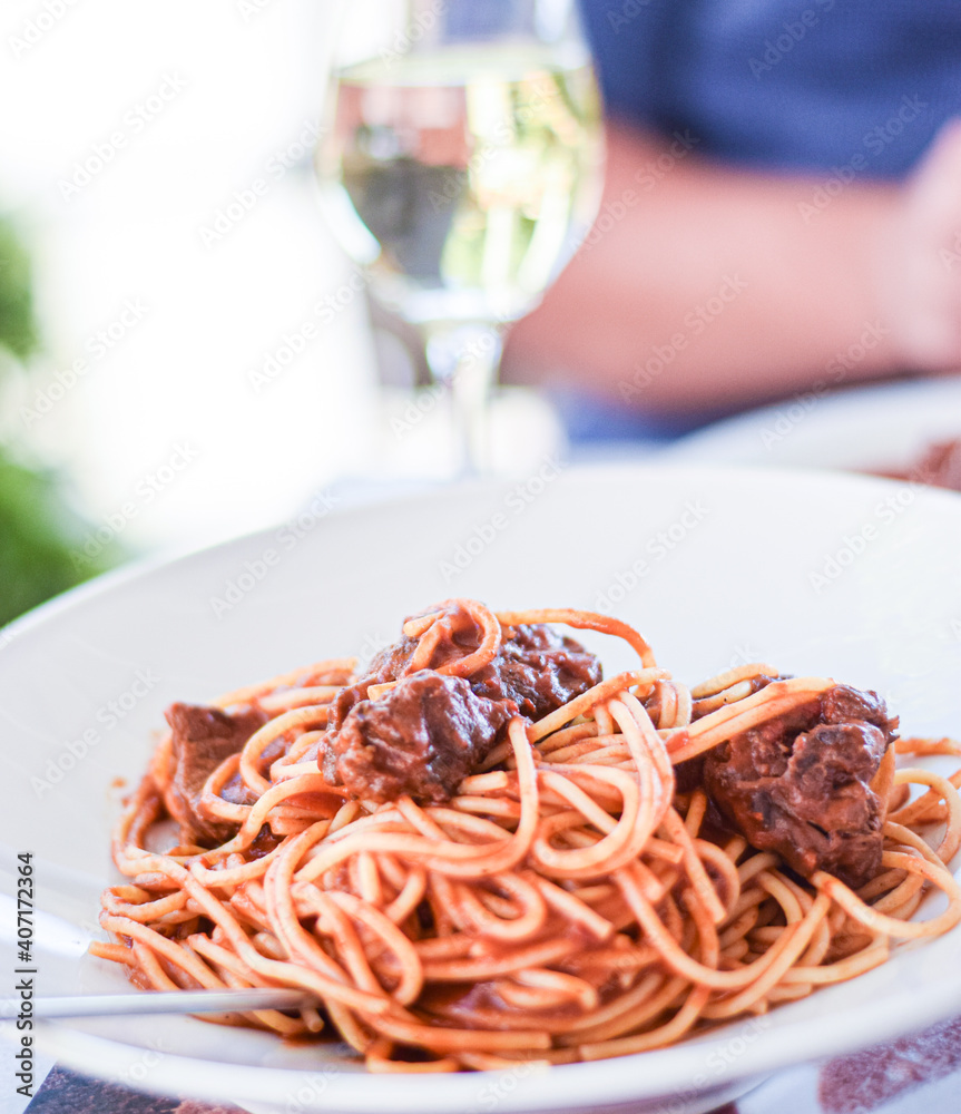 Poster Traditional spaghetti  with chunks of meat in a red bolognese sauce and spoon, outdoor eating background