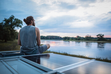 Man sitting on top of his camper van next to a river
