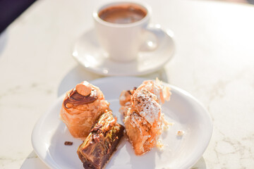 Chocolate, hazelnut and pistatio traditional greek baklava cakes served on a plate with coffee, outdoor café background