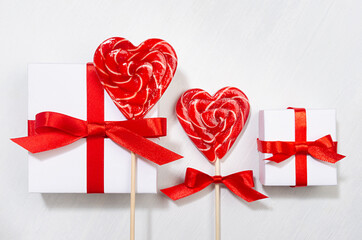 Bright birthday background with love - white gift boxes with red bow, lollipops hearts on white wood board, closeup.