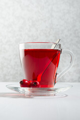 Red tea in elegant transparent cup with ripe hawthorn berries in sunlight on white wood table, vertical, closeup.
