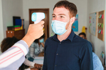Woman worker measuring body temperature of coworker at modern office - Focus on man face