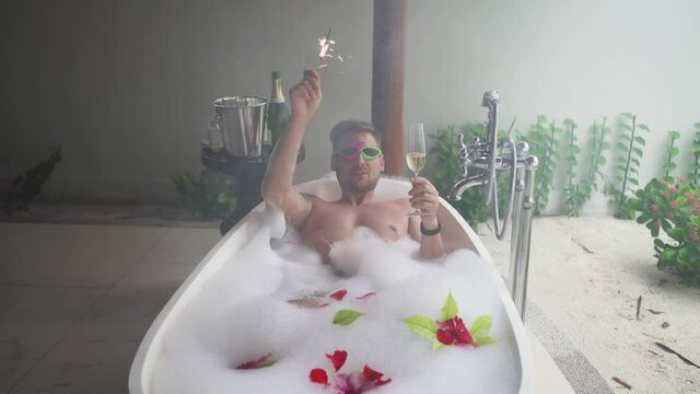 The blogger guy wishes you a Happy New Year or any other holidays, lying in a bath with foam and holding a glass of champagne in his hand brings his congratulations and a wish of health to everyone.