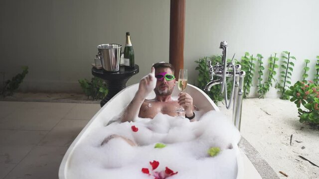 The blogger guy wishes you a Happy New Year or any other holidays, lying in a bath with foam and holding a glass of champagne in his hand brings his congratulations and a wish of health to everyone.