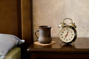 Alarm clock a cup of coffee standing on the bedside table near the bed.