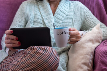 Relaxed woman on the sofa at home having a cup of coffee and checking her tablet