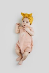 Astonished stylish baby in trendy clothes and yellow headband lying on gray background. Fashion...