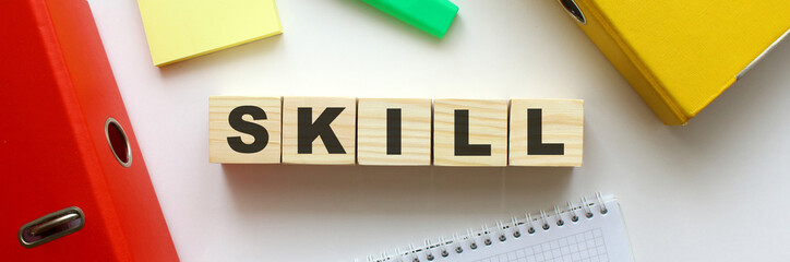Wooden cubes with word SKILL on the office desk. Folder and other office supplies.