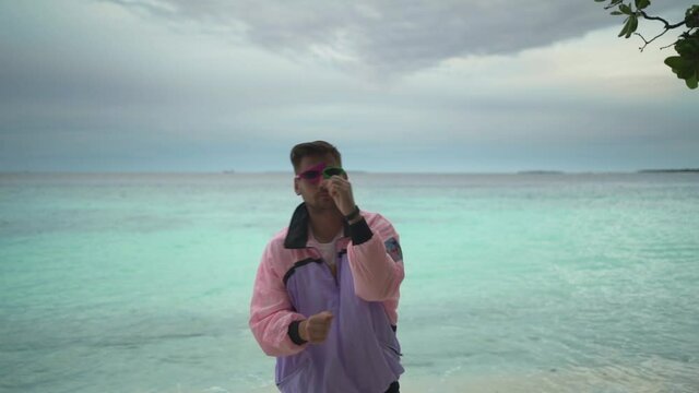 An unusual freak is dancing and having fun in front of the camera in clothes of the 80s and 90s against the background of the sea, a funny funny guy is happy and emotional.