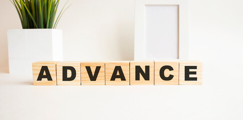 Wooden cubes with letters on a white table. The word is ADVANCE. White background.