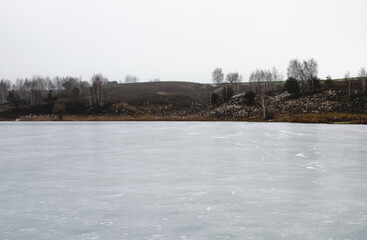 Frozen lake surrounded by hills without snow on a cloudy winter day