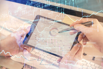 Double exposure of man's hands holding and using a phone and financial chart drawing. Market...