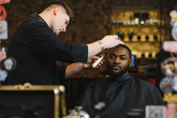 Portrait of young black man being trimmed with professional electric clipper machine in barbershop.Male beauty treatment concept. Young African guy getting new haircut in barber salon