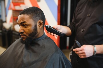 Closeup of process of trimming of hair in barber shop. Qualified barber keeping clipper in hands and correcting shape of hair to male client sitting on chair. Concept of haircut and shaving.