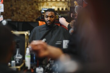 Obraz premium Black man in the barbershop. Cute black man makes a haircut in the African salon. Hair style. Haircut for adults.