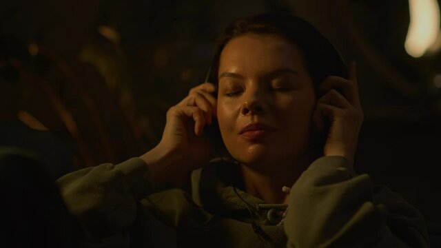 Beautiful girls starts listening to music, woman wear headphones, cozy evening 