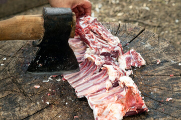 Butchering meat with an ax on a stump. A hand with an ax cuts the meat into pieces for further cooking. Natural food.