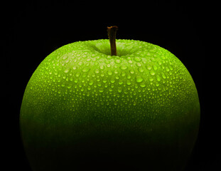 Bright green fresh apple with water droplets on it on a black background, perfect apple with dramatic abstract black background