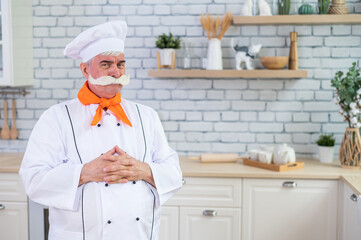 Portrait of an elderly male chef with bushy gray mustache in the kitchen.