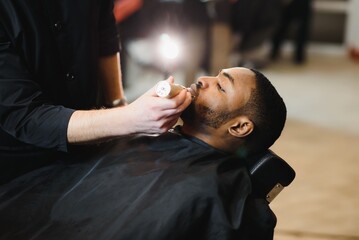 A barber is going through the electric cutting and shaving machine for the beard of an...