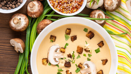 Mushroom cream soup on a wooden background with sliced mushrooms and onions.