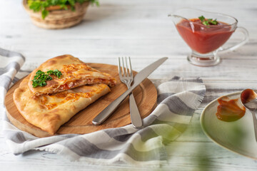 Calzone pizza on a wooden board. Served with tomato sauce and herbs