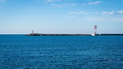 Sochi, Russia - November 25, 2020: Current city lighthouse on pier near sea station. Blue sky. Black Sea. Sunny autumn day.