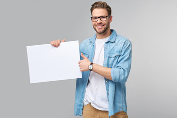 Portrait of a happy handsome young man holding blank white card or sign over white background