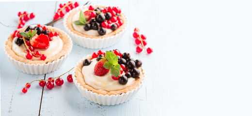 Homemade Tartlets with cream and fresh berries - ripe red and black currants, strawberries on blue rustic wooden background, top view.
