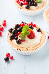 Homemade Tartlets with cream and fresh berries - ripe red and black currants, strawberries on blue rustic wooden background, top view.
